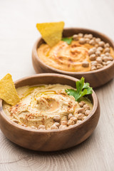 selective focus of delicious hummus with chickpeas and nacho in bowls on beige wooden table