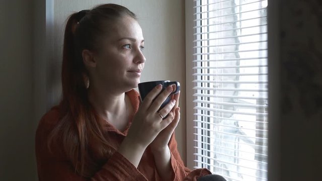 lifestyle woman sitting by the window with a mug of hot tea on a winter day