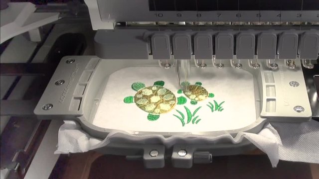 start  and stop of work of the embroidery machine with the green  thread   when performing work on the automated production of a colored design turtle and  grass on the white  background