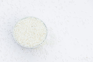 Milled rice in a cup and milled rice spread on a white ground