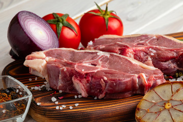Raw lamb meat on a wooden cutting board with spices and fresh vegetables.