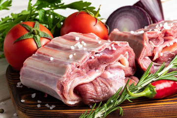 Raw meat. Beef ribs on a wooden cutting board with spices and fresh vegetables.