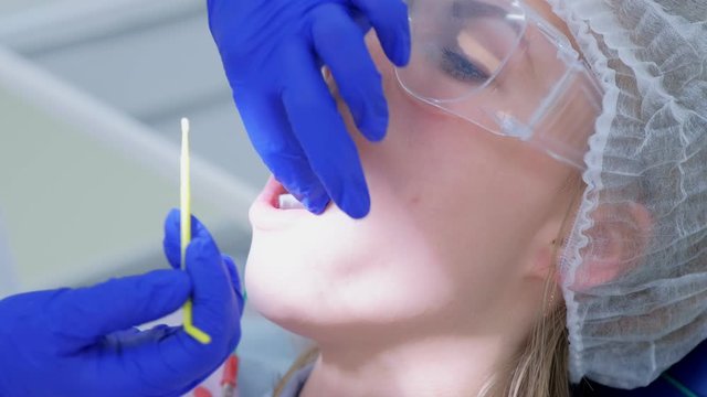 Dentist make fluoridation of teeth after ultrasonic cleaning for young woman. Stomatologist apply fluoride on patient's teeth. Portrait of young woman. Stomatology clinic, cure, treatment, procedure.
