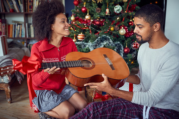 Couple in front of decoration Christmas tree. man surprise woman a with a guitar gift for Christmas.