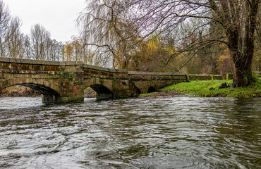 Fototapeta na wymiar View from a low perspective of the stone bridge over the River Wye, in full flood and bursting its banks, in the Derbyshire town of Bakewell