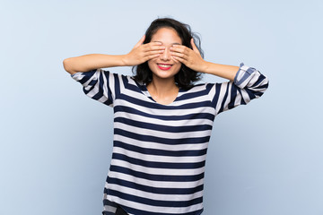 Asian young woman over isolated blue background covering eyes by hands