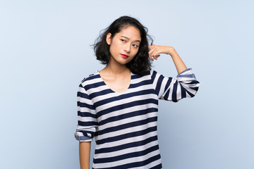 Asian young woman over isolated blue background making the gesture of madness putting finger on the...