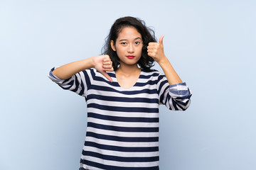 Asian young woman over isolated blue background making good-bad sign. Undecided between yes or not