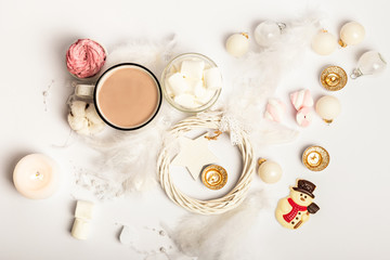 Hot cocoa with marshmallows and candles on a white background. New Year composition with white christmas tree decorations. Chocolate snowman.
