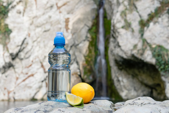 Blue bottle with sport-lock lid lemon flavored, on the background of a waterfall