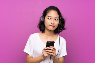 Asian young girl listening music with a mobile over isolated purple wall