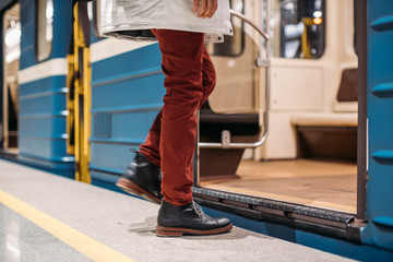 Well-dressed man in black shoes, red pants and white jacket enters into a subway train early in the morning. The left leg is blurred. Close up photo. Public transport and mobility in urban concept.