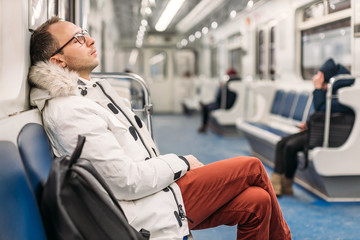 Handsome man with glasses in white jacket and maroon trousers fell asleep on the subway wagon on...