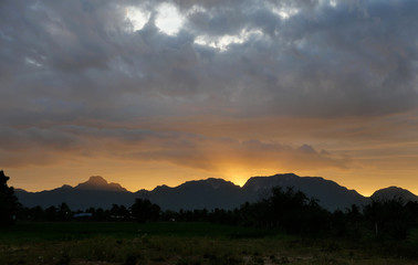 The silhouette of the mountain and trees with black and orange color fluffy cloud at sunrise, White cotton candy clouds on tropical blue sky at morning, Thailand