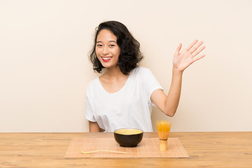 Obraz na płótnie Canvas Young asian girl with tea matcha saluting with hand with happy expression