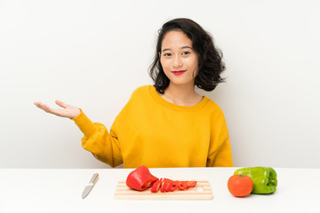 Young asian girl with vegetables in a table holding copyspace imaginary on the palm