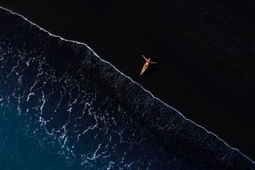 Top view of a woman in a red swimsuit lying on a black beach on the surf line, Coast of the island of Tenerife, Canary Islands, Spain,