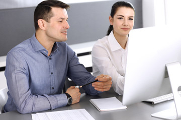 Cheerful smiling businessman and woman working with computer in modern office. Headshot at meeting or workplace. Teamwork, partnership and business concept