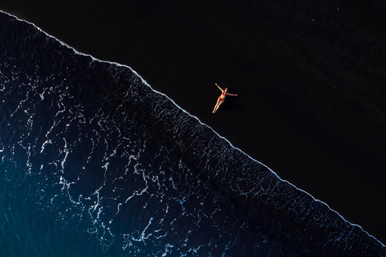 Top view of a woman in a red swimsuit lying on a black beach on the surf line, Coast of the island of Tenerife, Canary Islands, Spain,