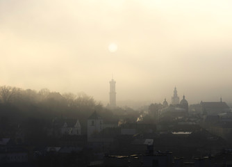 Historic center of Lviv in dense fog. Silhouette of the sun over the town hall. Ukraine