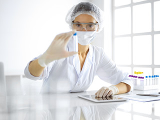 Professional female scientist in protective eyeglasses researching tube with reagents in...