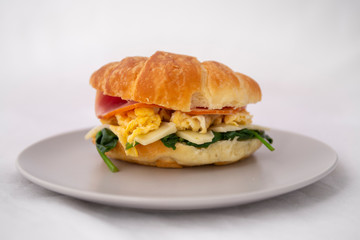 croissant sandwich of a ham, egg, spinach and avocado
