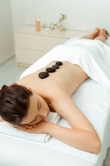 high angle view of attractive woman with hot stones on back lying on massage table in spa