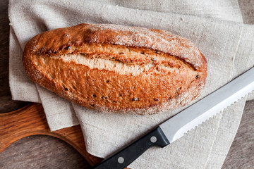 Loaf of whole wheat bread wooden board on kitchen table. Flat lay, top view