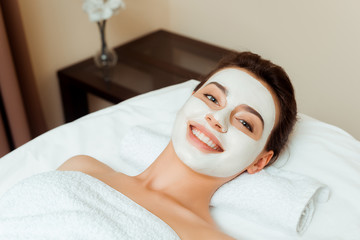 high angle view of smiling woman with mask on face lying on massage table in spa