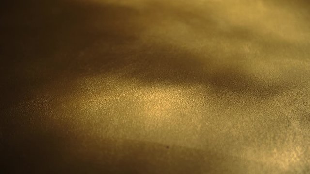 Organic and beautiful textured gold background. Slow rotation with light spots on plain surface. Metallic gold color, deep yellow, saturated, abstract, colorful and organically painted backdrop.