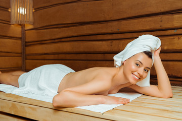 attractive and smiling woman in towels lying in sauna