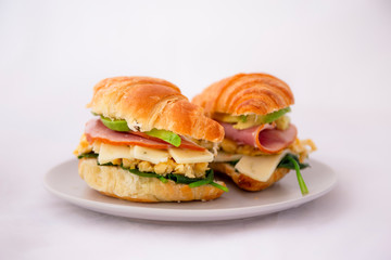 croissant sandwich of a ham, egg, spinach and avocado