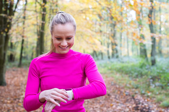 Woman Exercising In Autumn Woodland Looking At Activity Tracker On Smart Watch