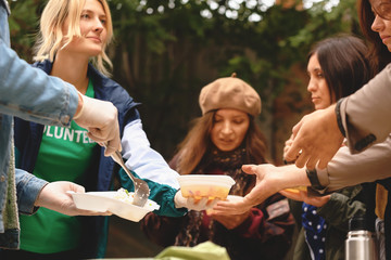 Volunteers giving food to homeless people outdoors