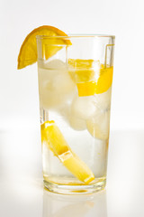 Glass of water with ice and slices of lemon on a white background.