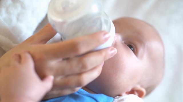 Baby holds mother&rsquo;s hand and drinks milk from a bottle, 4K