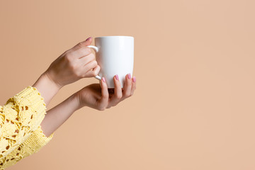 partial view of woman in yellow sweater holding cup of coffee, isolated on beige