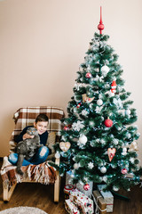 Happy little boy with cat Christmas gift box sitting near Christmas tree at home. Merry Christmas and Happy Holidays! Cute child indoors.