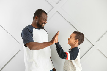 Obraz premium Portrait of African-American man and his little son giving each other high-five on light background