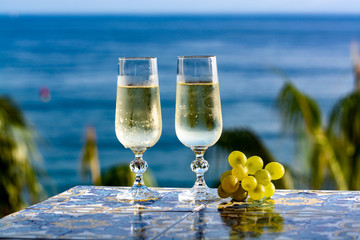 Romantic event, bottle with cold sparkling wine, cava or champagne served with two glasses on table with sea view and palm tree
