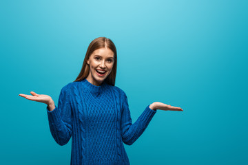 excited woman with shrug gesture in blue knitted sweater, isolated on blue