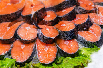 Salmon red fish steak at market. Raw fresh salmon steak as pattern background, close up. Large pile of fish meat with ice texture. Big organic heap of seafood farm salmon fish lined up for sale in