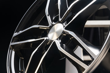 new expensive cast aluminum disc wheel black color, photographed on the tire. dark background, close-up. beautiful bending wheel spokes