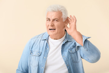 Mature man with hearing problem on light background