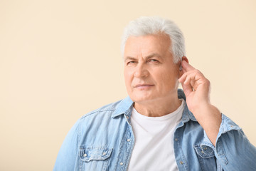Mature man with hearing aid on light background