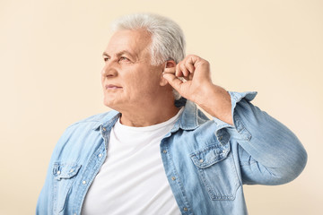 Mature man with hearing aid on light background