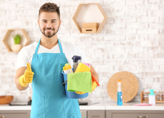 Male janitor with cleaning supplies showing thumb-up gesture in kitchen