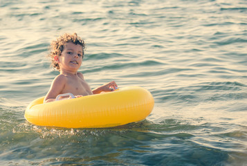 Happy Child on an yellow inflatable circle floating on the black sea. Copy space