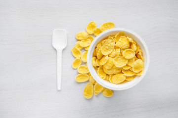Cornflakes in white bowl with spoon on white wooden background. Top view. Copy, empty space for text