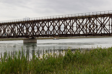 Old railway bridge over the river. Motor boat under the bridge. The reeds on the shore